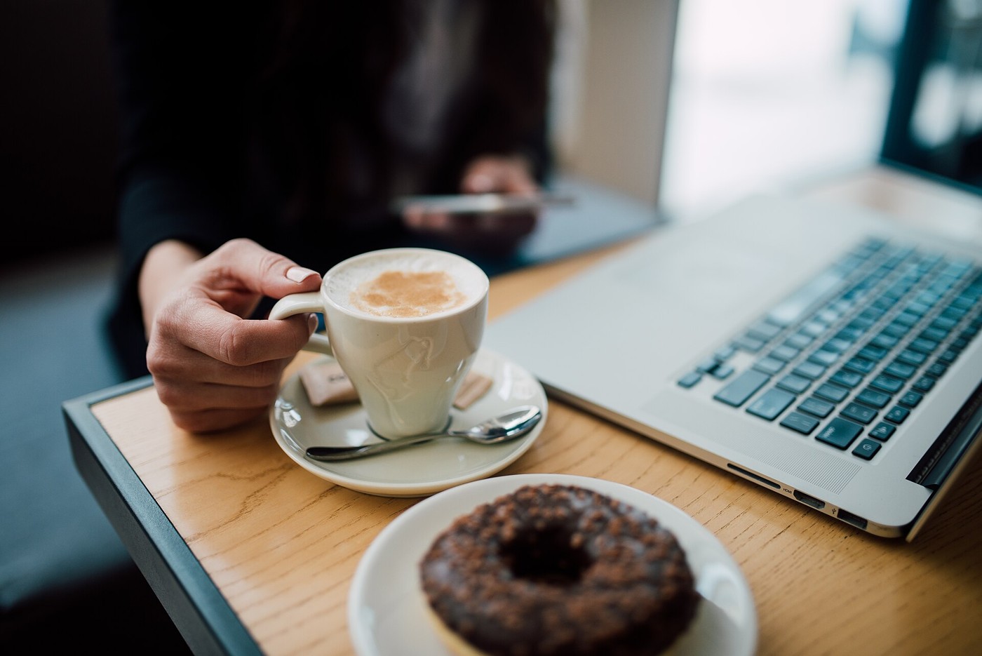 Person using a smartphone beside coffee and a laptop